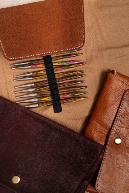 Set of colorful knitting needle tips on a brown leather case.
